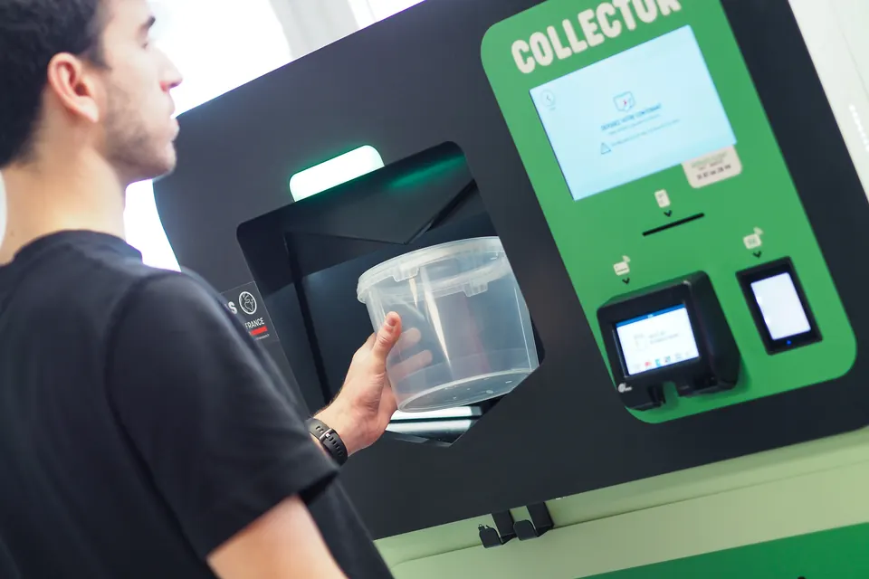 A customer returns a plastic deposit tray into the Collector