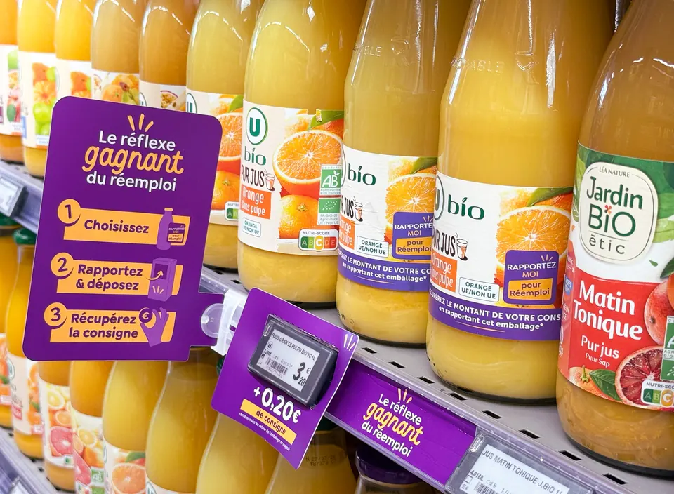 Rayon de jus en bouteilles réemployables, avec un panneau expliquant le geste